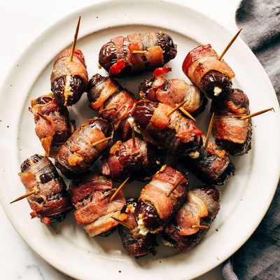 Bacon-wrapped dates on a plate with toothpicks in the dates.