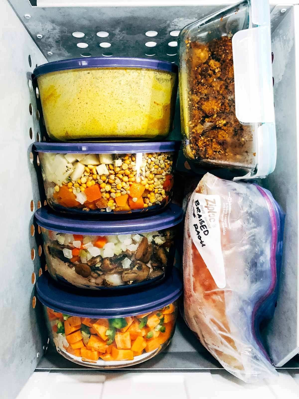 Various freezer meals in glass containers and plastic bags frozen in the freezer.